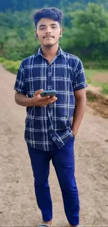 Young boy on a dirt path with greenery, holding a phone.