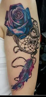 Blue rose tattoo with dreamcatcher design on arm, vibrant colors.