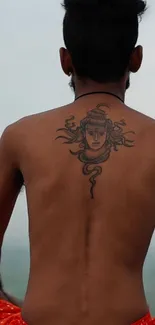 Back view of a man with a detailed tattoo in a serene setting.