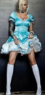 Tattooed woman in blue dress standing confidently with a dark background.