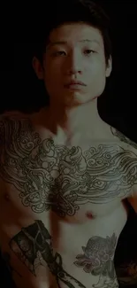 Tattooed male torso with intricate designs on a dark background.