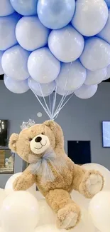 Teddy bear surrounded by blue and white balloons on fluffy clouds.