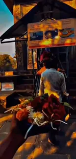 Hand holding flowers at temple entrance during sunset.