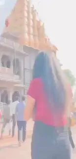 Woman in red shirt walking towards temple on a sunny day.