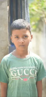 Young boy in green shirt stands in sunlight, looking thoughtful.