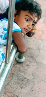 A thoughtful child with a calm expression by a metal railing.