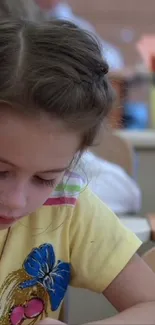 Young girl in yellow shirt focused in a classroom setting.