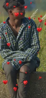 Young man in nature wearing plaid, sitting on a stone wall, surrounded by grass.