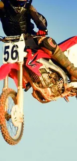 Dirt biker performs a high-flying jump against a blue sky backdrop.