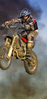 A motocross rider performs a dirt bike stunt against a smoky blue sky.