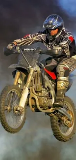 Motocross biker performing a high jump against a smoky sky background.