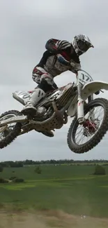 Motocross rider jumps in action against scenic countryside backdrop.