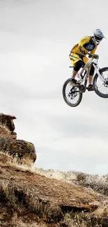 Biker in mid-air jumping off rocky terrain against clear sky.