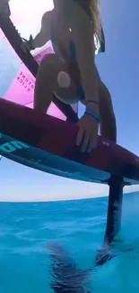 Woman windsurfing on blue ocean waves under clear sky.