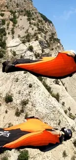 Two wingsuit flyers soaring over rocky mountains.