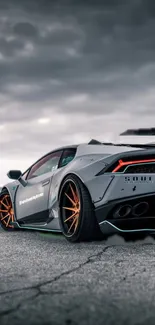 Gray sports car on pavement with cloudy sky backdrop.