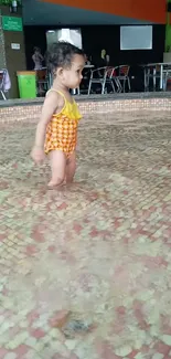 Toddler in yellow swimsuit splashing in a pool.