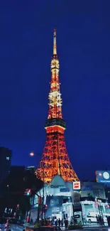 Tokyo Tower illuminated against a dark night sky, viewed from street level.