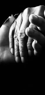 Two hands in black and white hold each other on a dark background.