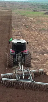 A tractor plowing a vast earthy field under a clear sky.