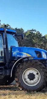 Blue tractor in a field under a clear sky with trees in the background.