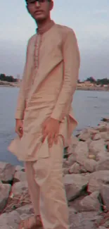 Person in beige traditional attire standing by seaside on rocky shore.