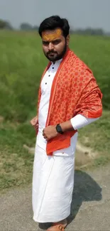 Man in traditional attire with orange shawl in nature.