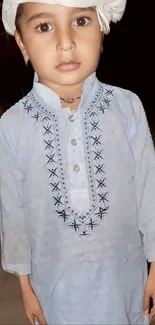 Child in traditional attire with intricate embroidery, light blue outfit.