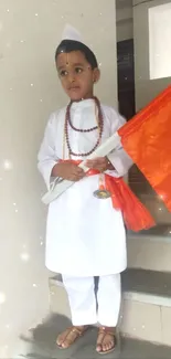 Child in traditional attire holding an orange flag while standing indoors.