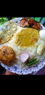 Bengali meal with rice, lentils, egg, and fish on a floral plate.