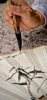 Hand painting traditional calligraphy on a bamboo-design fan.