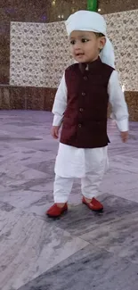 Young child in traditional attire with a maroon vest and white turban.