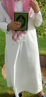 Person in traditional attire holding a book on a green lawn.