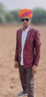 Man in maroon suit and orange turban outdoors.