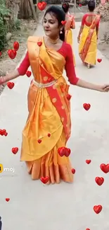 Woman in vibrant orange sari with heart designs dancing elegantly.