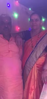 Couple in traditional Indian attire with colorful lights.