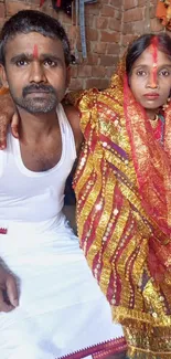 Traditional Indian wedding couple in colorful attire against a brick wall.