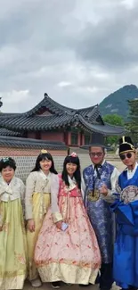 Five people in traditional Korean attire with historic architecture in background.