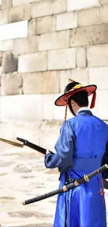 Traditional Korean guard in blue standing by stone wall.