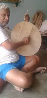 Elderly man playing a traditional drum in a rustic setting.