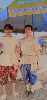 Two individuals in Cambodian attire under a market umbrella.