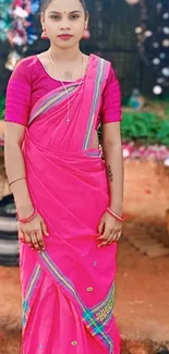 Woman in vibrant pink saree standing outdoors.