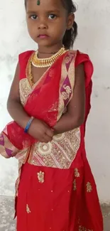 A child wearing a traditional red dress with gold designs and a matching headpiece.