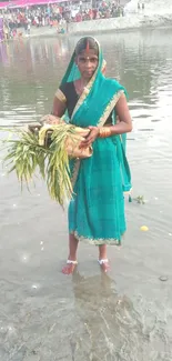 Woman in traditional attire performing ritual by a riverbank in vibrant setting.