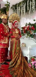 Couple in traditional wedding attire with floral background.