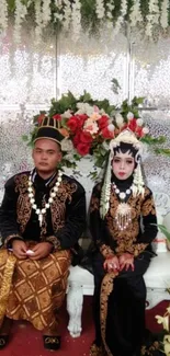 Traditional wedding couple in elegant attire with a floral backdrop.