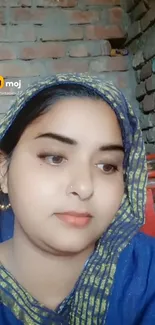 Portrait of a woman in blue traditional attire with a brick wall background.