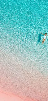 Aerial view of person floating in clear turquoise beach water with pink sand.