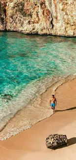 Man walks on serene beach with turquoise sea and sandy shore.