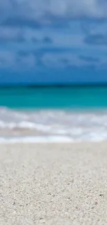 Serene beach scene with sand and ocean waves under a blue sky.